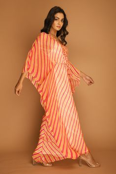 Carrot kaftan tunic with all-over Leheriya print, embroidered V-neckline and asymmetric hem. Comes with braided tie-up belt.
Component: 2
Printed, Embroidered
Neckline: V-Neck
Sleeve Length: Three Quarter
Fabric: Georgette
Color: Orange
Asymmetric hem
Braided belt with tassels - Aza Fashions Anarkali Style Maxi Kaftan For Spring, Summer Festive V-neck Kaftan, Summer Anarkali Maxi Kaftan, Summer Anarkali Style Maxi Kaftan, Floor-length Spring Festive Kaftan, Festive Beach Kurta In Maxi Length, Festive Beach Kurta Maxi Length, Festive Maxi Kurta For Beach, Summer Festive Floor-length Kaftan