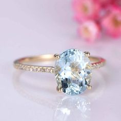 an oval cut aqua blue topaz ring with diamonds on the sides and a pink flower in the background