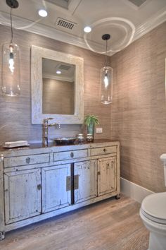 a white toilet sitting next to a bathroom sink under a mirror on top of a wooden floor