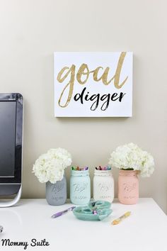 a desk with flowers, vases and a computer on it next to a sign that says goal digger