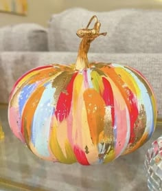 a colorful painted pumpkin sitting on top of a glass table next to a gray couch