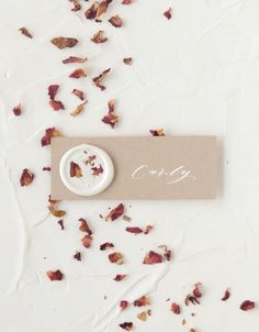 some dried rose petals and a button on a white surface with the word gone written in it