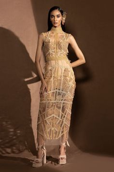 Dusk net fitted dress with high neck, embroidered gold metallic floral motifs and glass beads stripe pattern embellishment.
Component: 1
Pattern: Embellished and Embroidered
Type Of Work: Metallic Work and Glass Bead Cords
Neckline: High Neck
Sleeve Type: Sleeveless
Fabric: Net
Color: Beige
Other Details: 
Sheer illusion back
Back keyhole cut work button closure
Note: The headpiece and inner dress worn by the model is not for sale
Occasion: Cocktail,Party - Aza Fashions Gold Sleeveless Sequined Evening Dress, Gold Sleeveless Evening Dress With Sequins, Gold Sleeveless Evening Dress For Festive Occasions, Luxury Gold Sleeveless Dress, Gold Lace Evening Dress For Party, Luxury Lace Sleeveless Evening Dress, Gold Sleeveless Fitted Evening Dress, Gold Fitted Dress With Sheer Bodice, Fitted Gold Lace Dress