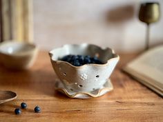 a white bowl filled with blueberries sitting on top of a wooden table next to a spoon