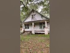 an old white house sitting in the middle of a field with trees and grass around it