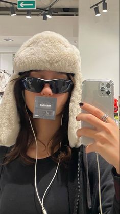 a woman wearing sunglasses and a furry hat is taking a selfie with her cell phone