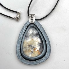 This teardrop shaped stone is wrapped in hand tooled leather which is painted in a complimentary color to the dark greys and black of the stone. Word Bracelet, Tiger Eye Bracelet, Dendritic Agate, Hand Tooled Leather, Complimentary Colors, Feather Necklaces, Agate Necklace, Tooled Leather, The Stone