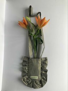 an orange flower is in a black and white checkered bag with straps hanging on the wall