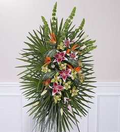 an arrangement of flowers and greenery in a white vase on a wooden table against a wall