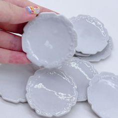 a hand is holding four white plates with designs on the rims and one has a painted fingernail