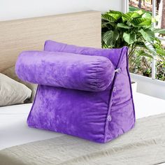 a large purple pillow sitting on top of a bed next to a potted plant