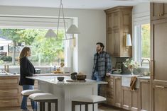 a man and woman standing in a kitchen next to an island with stools on it