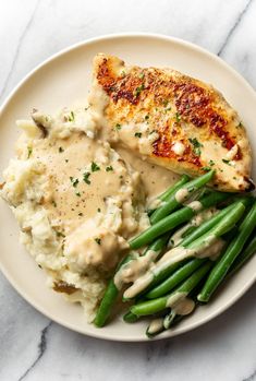 a white plate topped with green beans and mashed potatoes covered in gravy