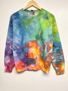 a colorful tie - dyed sweatshirt hanging on a hanger against a white wall,