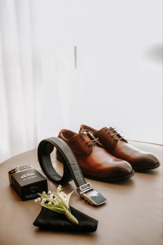 a pair of brown shoes and a black tie on top of a table next to a cell phone