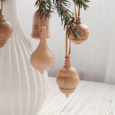 three wooden ornaments hanging from a tree branch in a white vase on a wood table