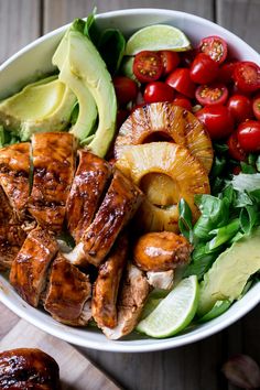 a bowl filled with meat, vegetables and avocado on top of a wooden table