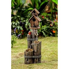 a bird house made out of logs in the grass with a red bird perched on top