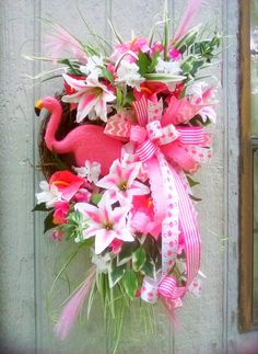 a pink flamingo wreath with white lilies and pink flowers in front of a door