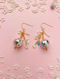 These 14K gold-plated disco ball dangle earrings with star and faux crystal charms are the perfect accessory for a raucous night out. Whether you want to dance with somebody or dance all by yourself, these maximalist beauties will catch light and shine bright. They also make the perfect gift for your dance-aholic bestie or a diva bachelorette.  Drop Length: 2 inches Care Instructions: These earrings are handmade with nickel-free gold-plated stainless steel. Gold-plated jewelry is susceptible to tarnishing if exposed to lotion or oils, so I recommend moisturizing and adding any fragrance before wearing. * Due to different settings on computer monitors and mobile devices, colors that appear on your screen may vary slightly from the actual product. Love this? Check out more Offkilter Co jewel Disco Ball Jewelry, 70s Jewelry Disco, Maximalist Earrings, New Years Jewelry, Disco Jewelry, Silver Disco Ball, Star Festival, 70s Jewelry, Queen Outfit