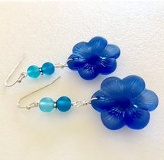 "Beautiful light sapphire blue or royal blue sea glass flowers are the feature of these pretty dangle earrings. Large 1\" sea glass flower is accented with contrasting shades of royal blue, teal and aqua blue sea glass rounds. Earrings are made of cultured tumbled sea glass and wire wrapped in German silver plated jeweler's wire. They hang from silver plated ear wires. Light sapphire blue earrings measure 2\" long and royal blue are 2 1/4\" long. Also available in Sterling silver. Listing is for Blue Flower-shaped Jewelry For The Beach, Blue Flower Jewelry For The Beach, Blue Sea Glass Nickel Free Earrings, Blue Sea Glass Nickel-free Earrings, Nickel-free Blue Sea Glass Earrings, Blue Czech Glass Beach Jewelry, Blue Flower Earrings Nickel Free, Handmade Blue Sea Glass Earrings, Blue Recycled Glass Dangle Earrings