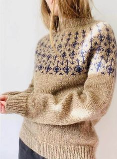 a woman is wearing a sweater with blue and white designs on the back, she has her hands in her pockets