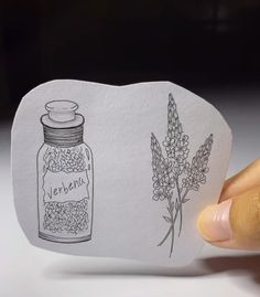 a hand holding up a piece of paper with an image of a jar and flowers on it