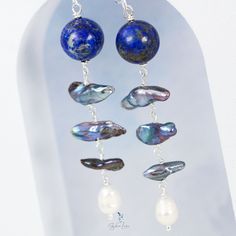 Add a touch of elegance to your jewelry collection with these stunning Lapis Lazuli and freshwater pearl drop earrings. The design features a 12 mm natural Lapis Lazuli stone bead, accompanied by a chain of 3 blue pearls and a white freshwater baroque pearl at the end. Made with solid 925 sterling silver ear wires, wires, and eye pins, these earrings make a thoughtful and beautiful gift for your loved ones. Don't miss out on adding these unique and exquisite earrings to your collection! Material Teardrop Pearl Earrings With Natural Stones, Pearl Dangle Earrings With Natural Stones, Natural Stone Dangle Pearl Earrings, Blue Pearl Charm Drop Earrings, Handmade Baroque Pearl Dangle Jewelry, Long Drop Pearl Earrings With Dangling Beads, Elegant Pearl Earrings With Dangling Beads For Gift, Elegant Round Earrings With Dangling Beads, Long Drop Pearl Earrings For Gift