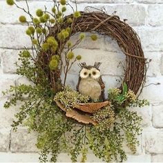 an owl is sitting in the middle of a wreath with greenery around it on a brick wall