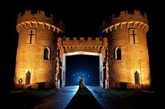 a bride and groom standing in front of a castle at night with the lights on