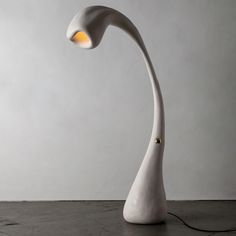 a white floor lamp with an orange light on it's side and a gray wall in the background