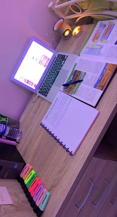 an open laptop computer sitting on top of a wooden desk next to a pile of books