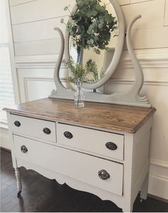 a white dresser with drawers and a mirror on the wall above it, next to a plant in a vase