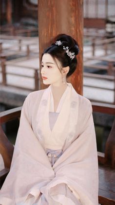 a woman sitting on top of a wooden bench wearing a white dress and headpiece