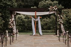 an outdoor wedding ceremony setup with white drapes and flowers on the aisle, surrounded by greenery