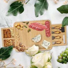 a wooden cutting board topped with cheese, meat and nuts next to flowers on a table