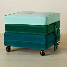 a green and blue ottoman sitting on top of a wooden floor next to a white wall