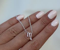 a woman's hand holding a silver necklace with the letter m on it