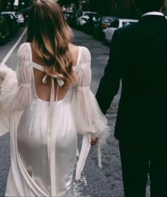 a man and woman are walking down the street holding hands, dressed in white dresses