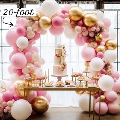 a table topped with a cake surrounded by pink and gold balloons in front of a window