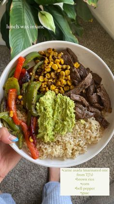 a person holding a white bowl filled with rice and veggies next to a plant