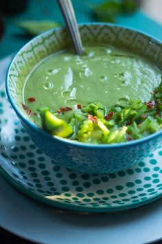 a blue bowl filled with broccoli soup on top of a white and green plate