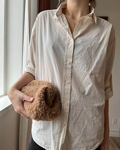 a woman holding a teddy bear in her right hand while standing next to a window