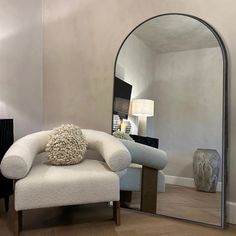 a white chair sitting next to a large mirror in a living room on top of a hard wood floor