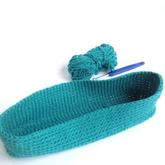 a blue knitted headband with a ball of yarn next to it on a white surface