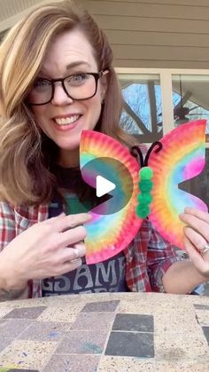 a woman holding up a colorful butterfly shaped paper plate in front of her face and smiling at the camera