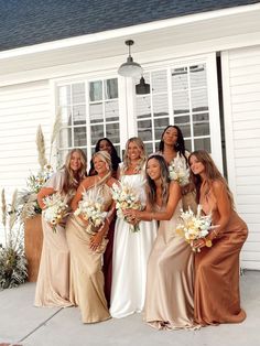 a group of women standing next to each other in front of a white house holding bouquets