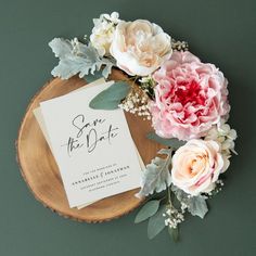 the save the date card is placed on top of a wood slice with flowers and greenery