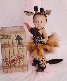 a baby dressed as a giraffe standing next to a cardboard box