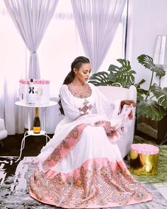 This stunning dress is a true masterpiece of Ethiopian textile art. The lower part of the dress is made from shimena, a handwoven fabric known for its intricate patterns and rich texture. The shimmering material adds a touch of elegance and movement to the dress, making it perfect for special occasions. The dress is adorned with light pink tilf embroidery, a traditional Ethiopian technique that involves intricate and colorful designs stitched onto fabric. The tilf embroidery on this dress is par Modern Ethiopian Dress, Pink Habesha Kemis, Habesha Clothes, Ethiopian Dresses, Eritrean Clothing, Eritrean Dress, Ethiopian Clothing, Habesha Dress, Ethiopian Traditional Dress